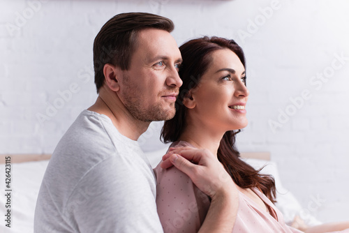 Man embracing smiling brunette wife in bedroom