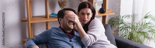 Scared woman covering eyes to husband on couch, banner