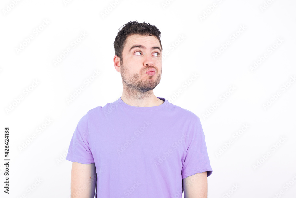 Obraz premium young handsome caucasian man wearing purple t-shirt against white background, looks pensively aside, plans actions after university, imagines what to do Thinks over about new project.