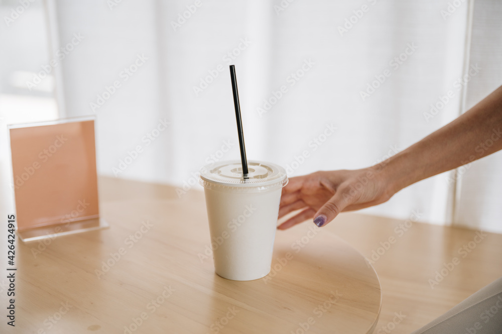 Hand of woman holding disposable coffee cup on wooden table with empty label in cafe Hand of woman holding disposable coffee cup on wooden table with empty label in cafe