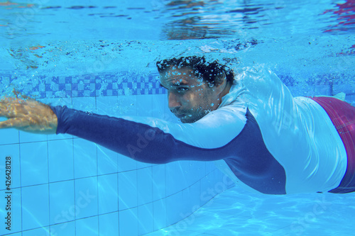Man swimming in blue water. Swimming man underwater photo. Swimming pool training for slimmering body. Underwater male swimwear. Blue pool water with bubbles