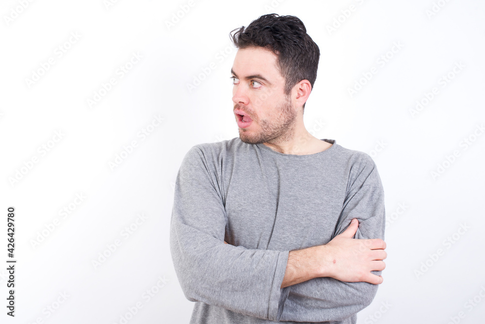 Astonished young handsome caucasian bearded man wearing pyjama over white wall looks aside surprisingly with opened mouth. Astonished young handsome caucasian bearded man wearing pyjama over white wall looks aside surprisingly with opened mouth.