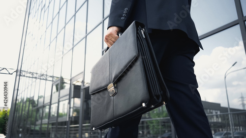 cropped view of businessman walking with leather briefcase. photo