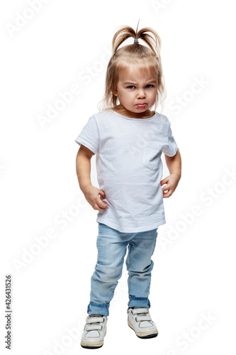 Angry little girl 2 years old in jeans and a white T-shirt. Anger, aggression and resentment. Isolated on white background. Vertical. Full height.