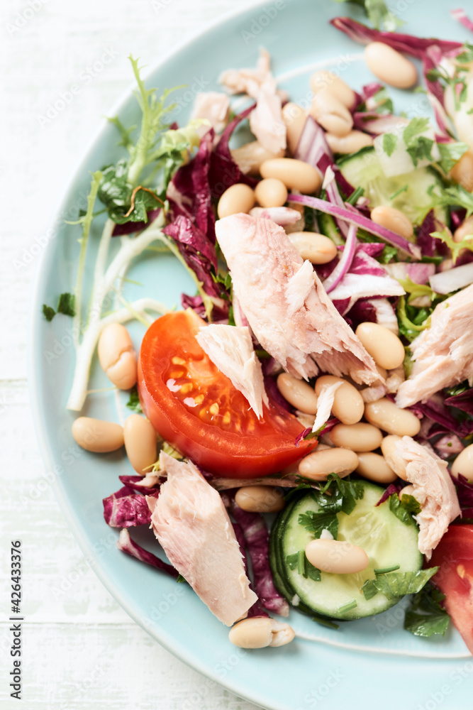Tuna salad with tomatoes, cannelloni bean and endive. Bright wooden background. Top view. Close up. Tuna salad with tomatoes, cannelloni bean and endive. Bright wooden background. Top view. Close up.