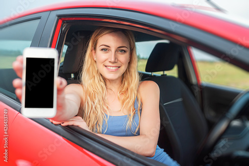 Woman in car shows smartphone with blank screen.