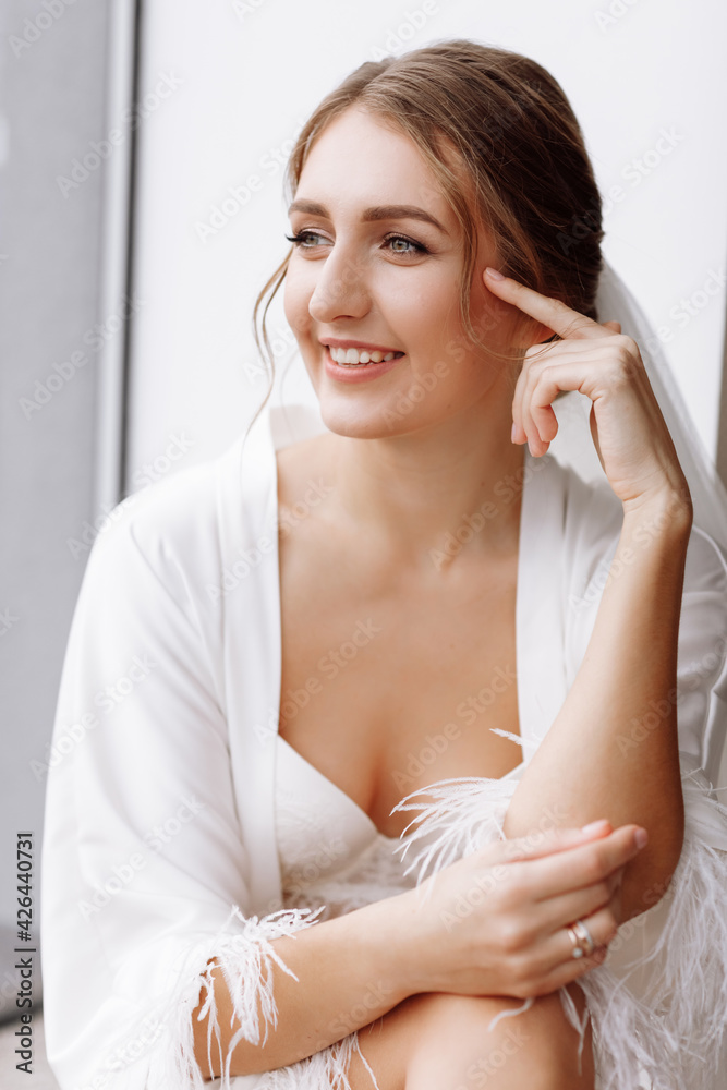 Morning of bride. Gorgeous bride. beautiful woman with long hair in a white robe at the window.the morning of the bride before the wedding. Natural beauty and professional make-up. skin care products Morning of bride. Gorgeous bride. beautiful woman with long hair in a white robe at the window.the morning of the bride before the wedding. Natural beauty and professional make-up. skin care products