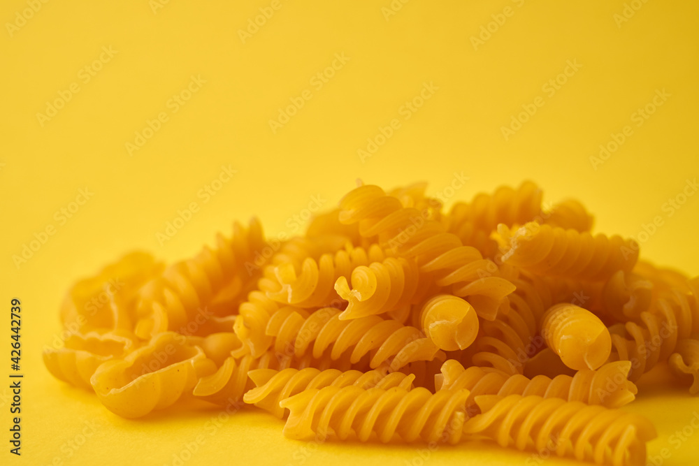 Pasta in the form of spirals and shells on a yellow background.