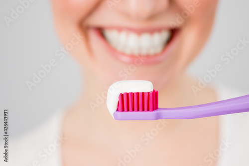 A woman with a snow-white smile holds a toothbrush with paste on a white background