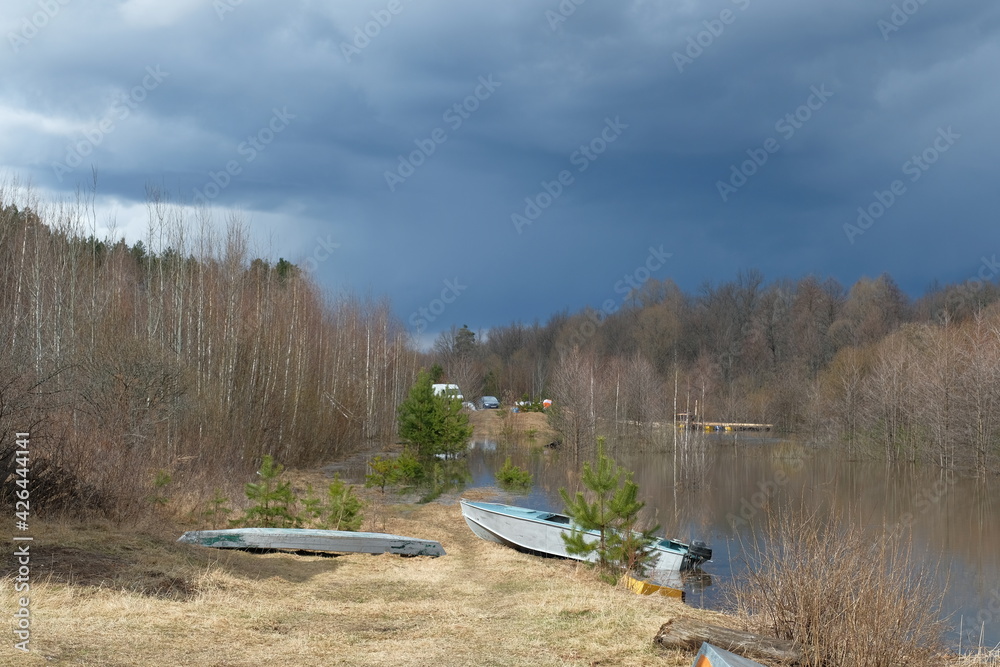 Naklejka premium River bank, spring, day, blue sky. There are boats on the shore.