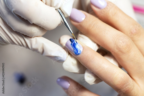 Nail design. The process of coating the nails with gel polish and drawing the design with a brush by a specialist in a beauty salon. Close-up. Space for text