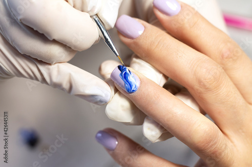 Nail design. The process of coating the nails with gel polish and drawing the design with a brush by a specialist in a beauty salon. Close-up. Space for text