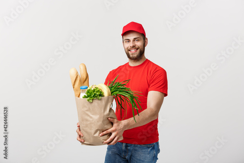 Delivery Concept - Handsome Cacasian delivery man carrying package bag of grocery food and drink from store. Isolated on Grey studio Background. Copy Space. photo