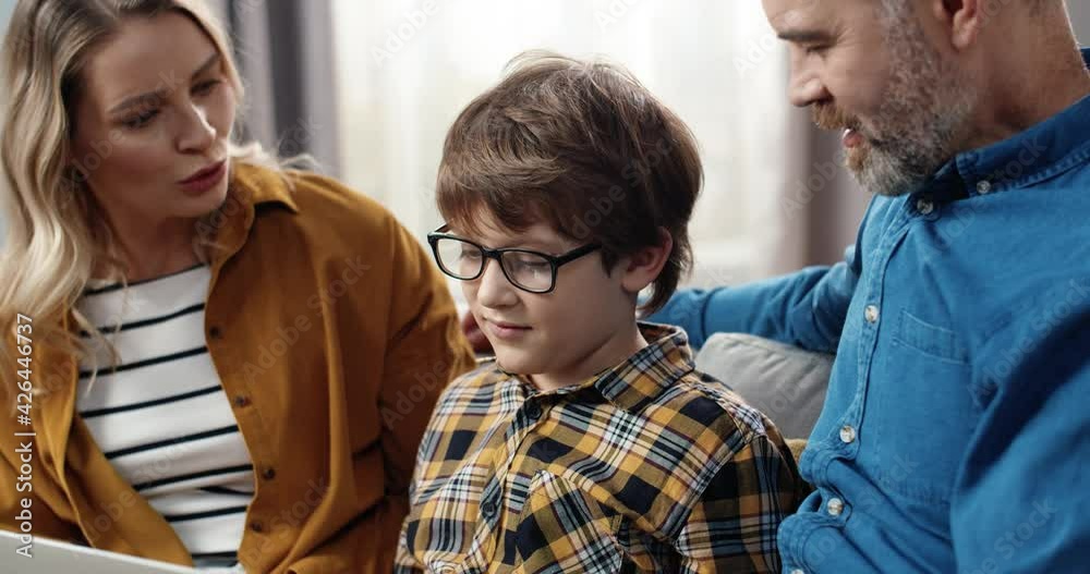 Happy parents admire the computer knowledge of their school-age son and praise him sitting together on couch at home. Happy parents admire the computer knowledge of their school-age son and praise him sitting together on couch at home.
