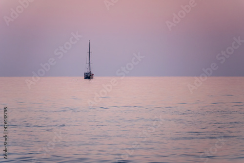 Sailing yacht in the blue sea during beautiful pink sunset.
