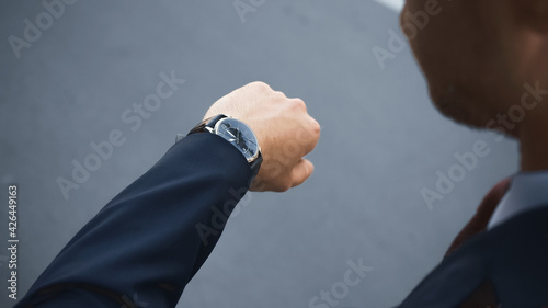 cropped view of businessman in formal wear looking at wristwatch while waiting outside.