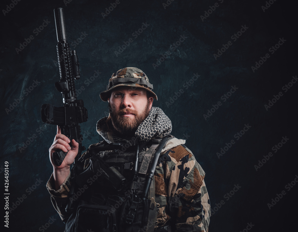 Serious guy in camouflage costume holding a rifle in dark background Serious guy in camouflage costume holding a rifle in dark background