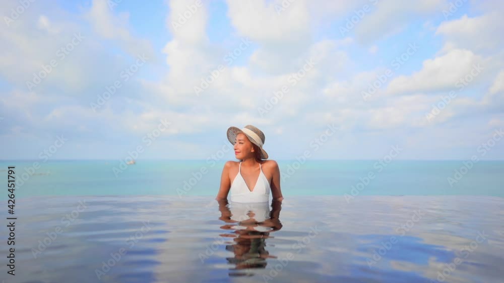 Asian skinny woman enjoying the sea view from the inside infinity pool front view daytime cloudscape Asian skinny woman enjoying the sea view from the inside infinity pool front view daytime cloudscape