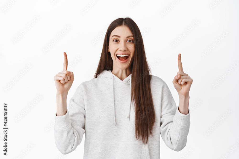 Happy laughing girl pointing fingers up, demonstrate banner on top, showing cool advertisement or logo, display at item above, standing against white background Happy laughing girl pointing fingers up, demonstrate banner on top, showing cool advertisement or logo, display at item above, standing against white background