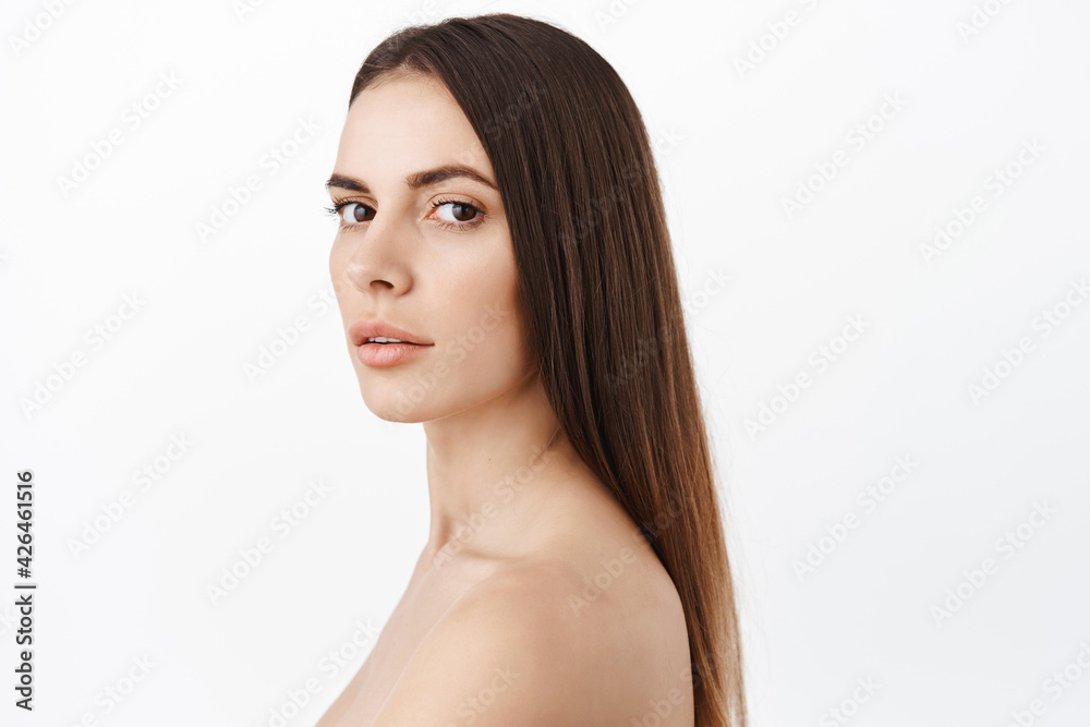 Fototapeta premium Beautiful woman with healthy long brunette hair, clean smooth skin, hydrated facial without wrinkles, anti-aging effect of cosmetics, turn head and look fashion, white background