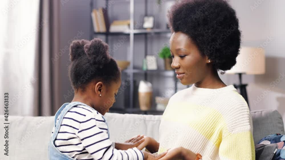Close up of happy cute African American little adorable girl playing with young mom clapping hands spending time together in living room. Side view of female parent having fun with small kid Close up of happy cute African American little adorable girl playing with young mom clapping hands spending time together in living room. Side view of female parent having fun with small kid