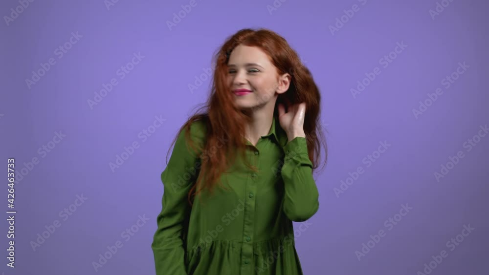 Attractive woman with red long hairstyle dancing on violet studio background. Girl in green dress. Positive mood. Attractive woman with red long hairstyle dancing on violet studio background. Girl in green dress. Positive mood.