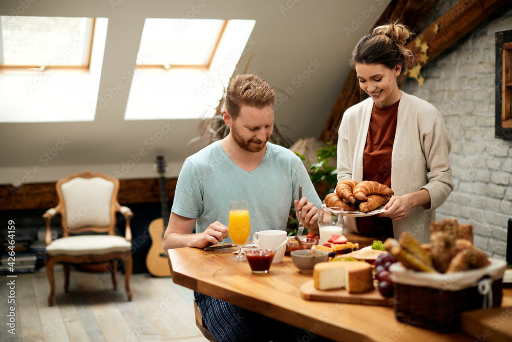 Happy woman serving croissants while having breakfast with her boyfriend at home. Happy woman serving croissants while having breakfast with her boyfriend at home.