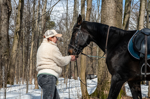 woman in beige jacket and cap with black horse in spring park 