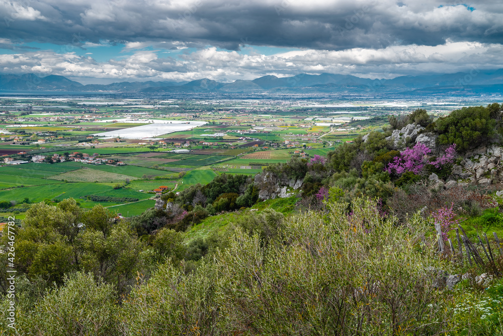 A stunning landscape of southern Italy from a high hill, Madonna del Granato Sanctuary, in April, when the fields emerge green. The valley is lined with roads, many trees, shrubs and houses