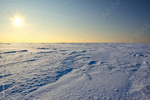 The sky is colored by the sun over a snow covered plain of fields