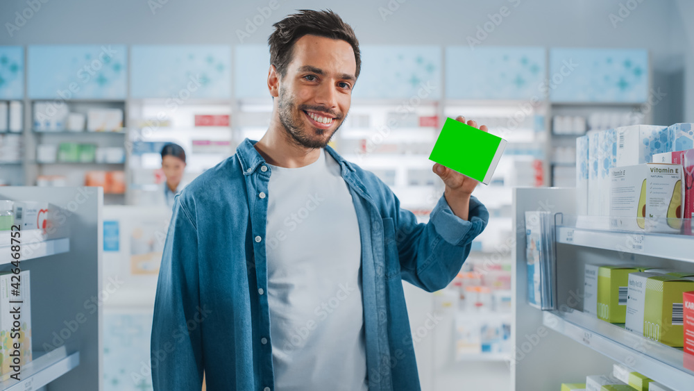 Pharmacy Drugstore: Portrait of Handsome Latin Man Holding Mock-up Template Medicine Package with Green Template, Looking at Camera, Smiling Happily. Customer Recommending Best Product