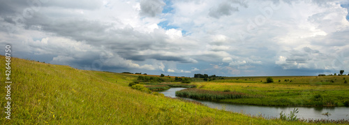 Summer panoramic landscape with dark stormy clouds over the calm river and green meadows.Russian rural landscape.