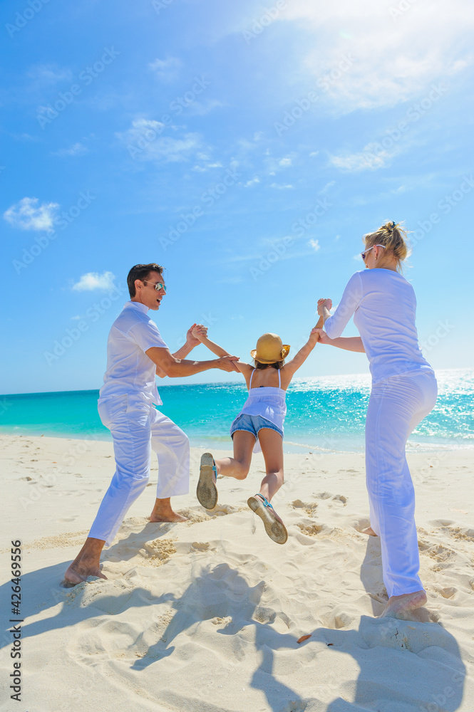 Family at the beach, mother, father and daughter playing on the sand dressed in white tropical outfits Family at the beach, mother, father and daughter playing on the sand dressed in white tropical outfits