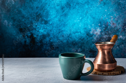 Make coffee in a Turk. Copper turk and ceramic mug. Bright blue background. Front view.