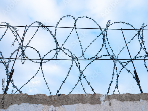 Barbed wire on the concrete fence, close-up, against the blue sky. Protected area.