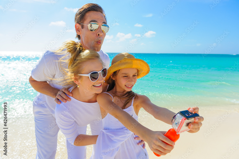 Family at the beach, mother, father and daughter taking photos, playing on the sand dressed in white tropical outfits Family at the beach, mother, father and daughter taking photos, playing on the sand dressed in white tropical outfits
