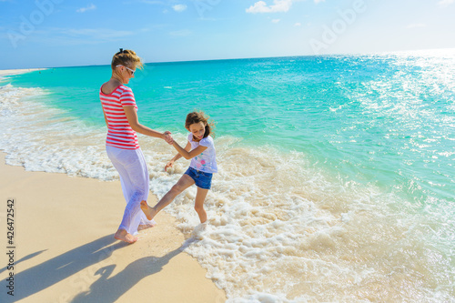 Family at the beach, mother and daughter walking and holding hands on the shoreline in tropical outfits