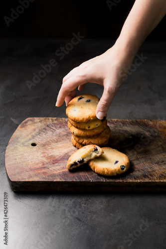 A woman’s hand taking one tasty blueberry cookie on a wooden table with a black stone texture in the background photo