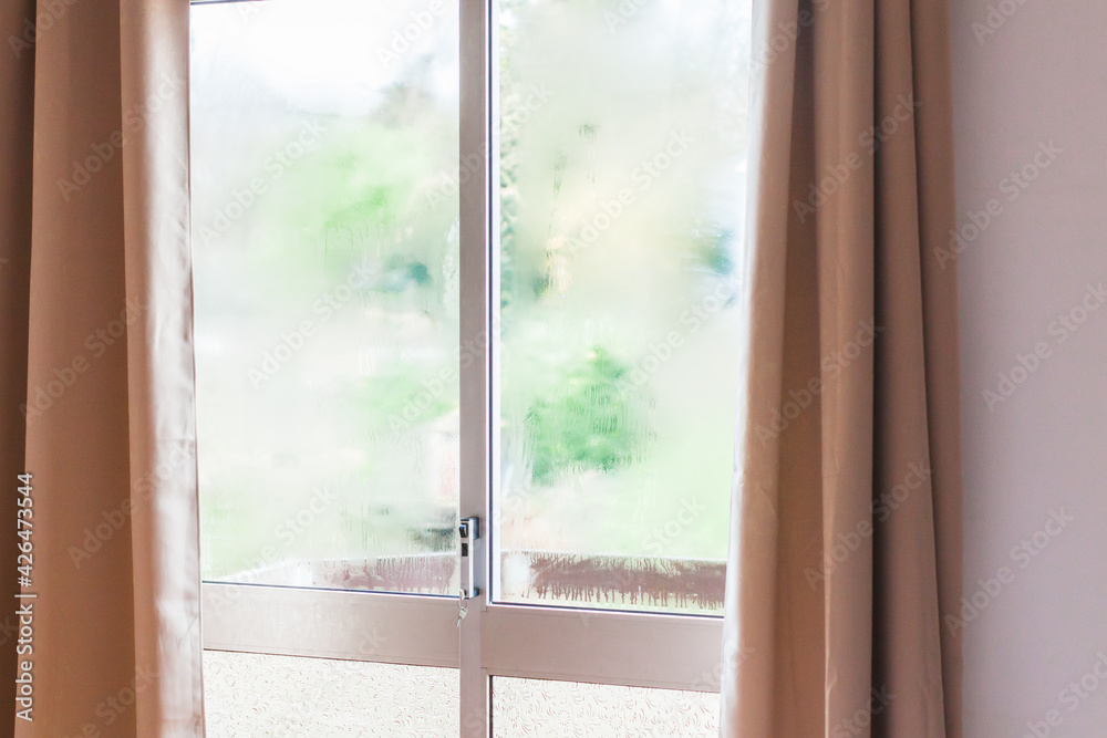 Fototapeta premium Window with condensation of steam after heavy rain. Bright morning sun in the window through the curtains. Texture or background photo, copy space