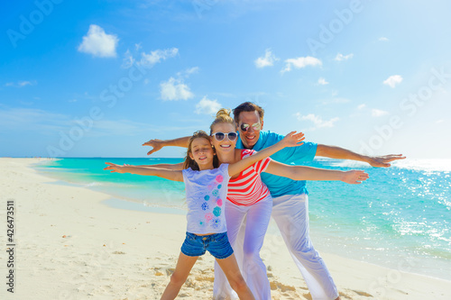 Family at the beach, mother, father and daughter playing on the sand dressed in colorful tropical outfits