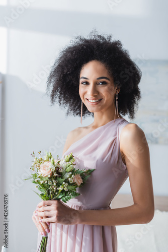 Εκτύπωση καμβά Elegant African American bridesmaid smiling at camera while holding wedding bouquet