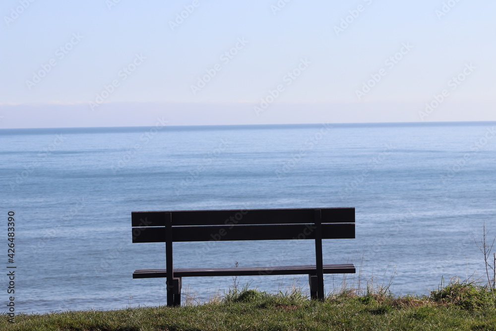 A wooden bench situated on a cliff with views out to the blue sea 