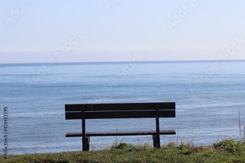 A wooden bench situated on a cliff with views out to the blue sea 