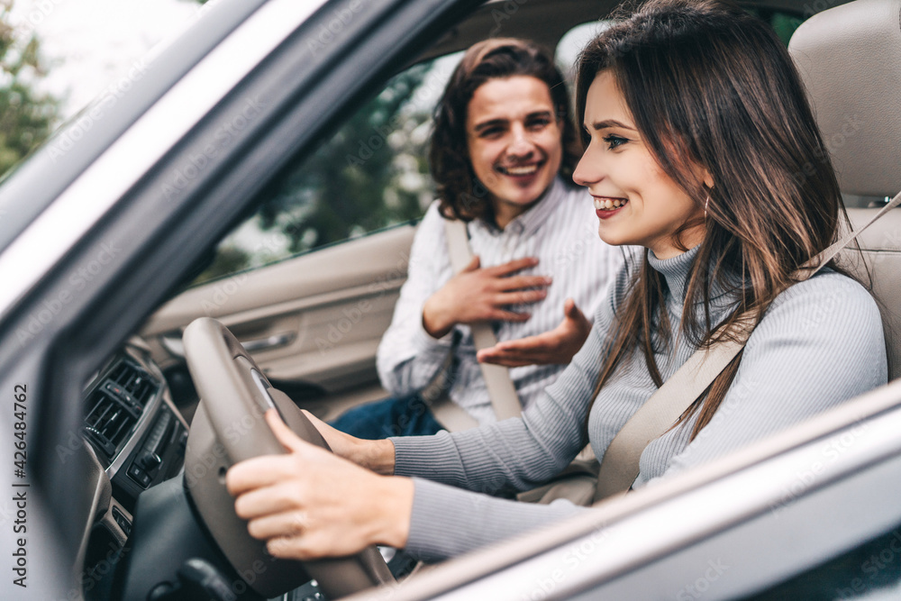 Cheerful young couple in front of the car during a road trip talking and smiling at each other. Driving safety