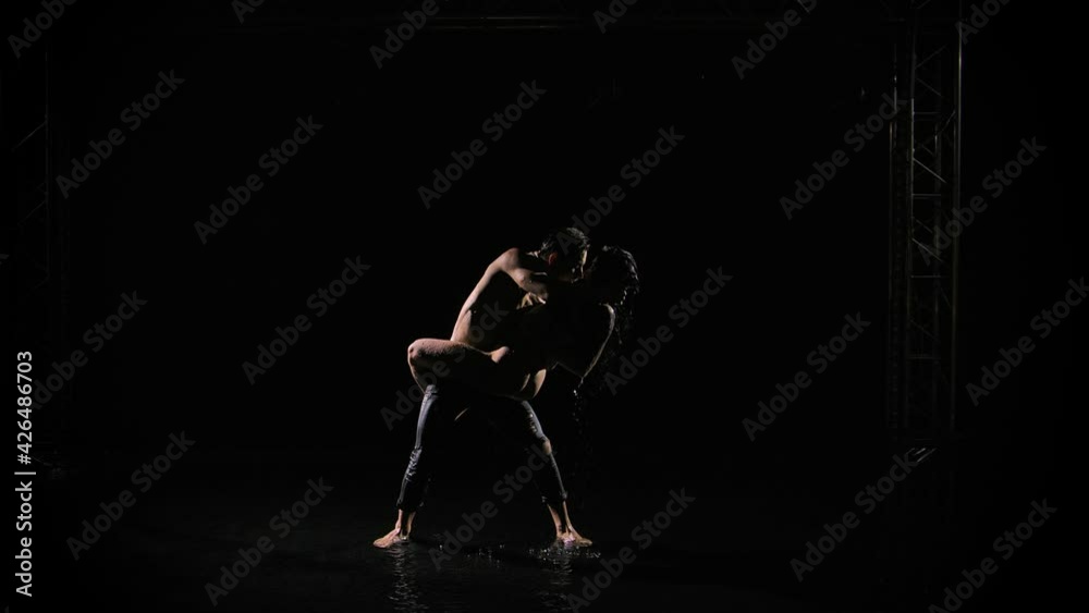 Happy lovers perform dance of passion in rain and enjoy each other. Water runs down wet bodies and sparkles in the studio light. Love story of a happy couple. Silhouettes of naked bodies. Slow motion. Happy lovers perform dance of passion in rain and enjoy each other. Water runs down wet bodies and sparkles in the studio light. Love story of a happy couple. Silhouettes of naked bodies. Slow motion.