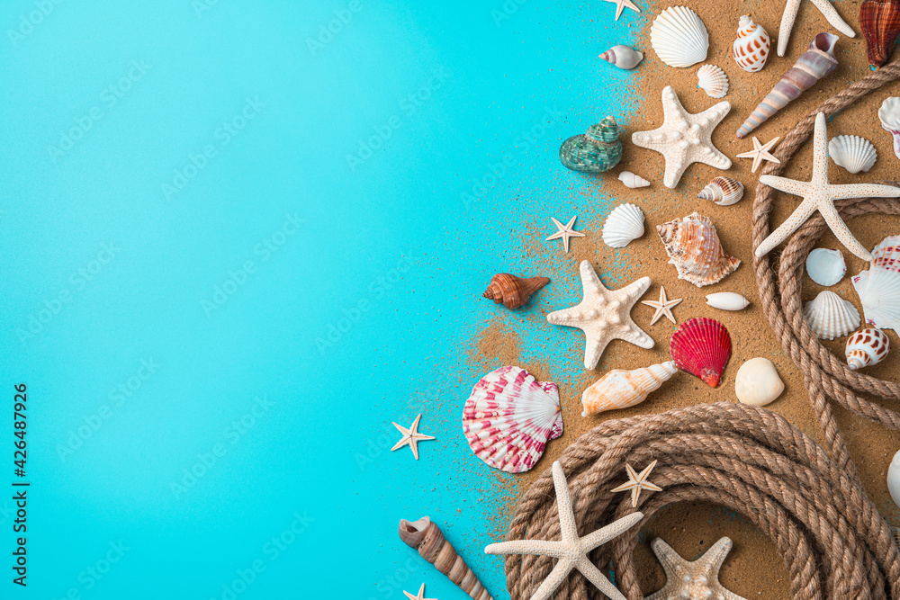 Naklejka premium Seashells of various kinds, starfish and a rope on the sand on a blue background.