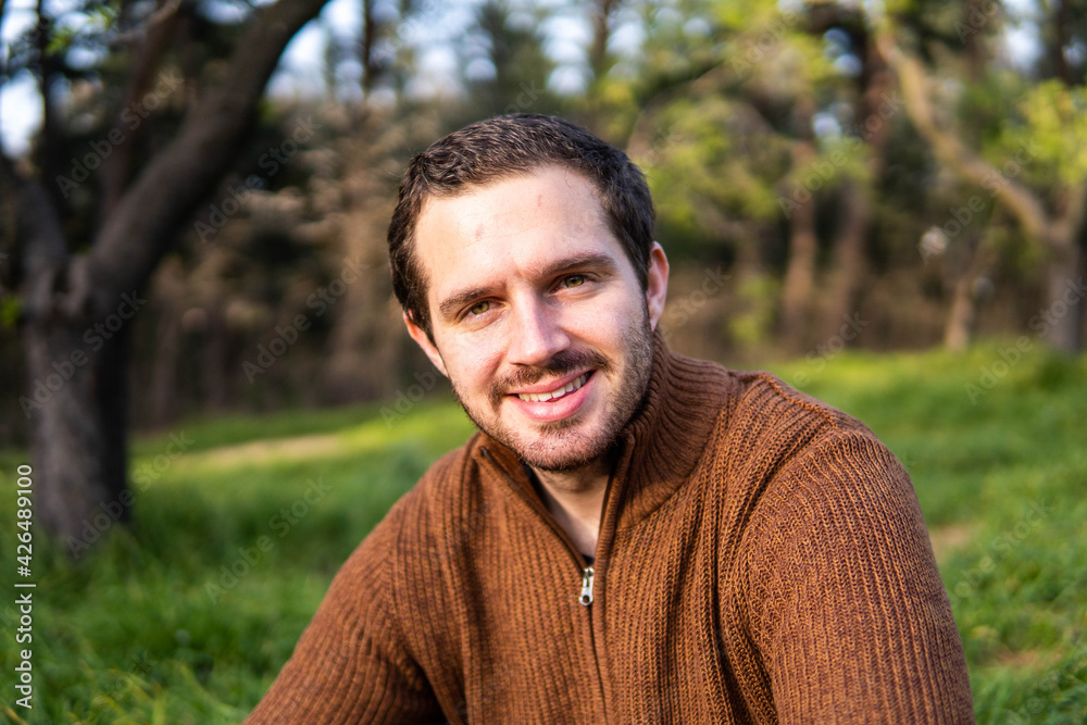 Photo of a young and attractive man sitting in the park during a sunny day and smiling Photo of a young and attractive man sitting in the park during a sunny day and smiling