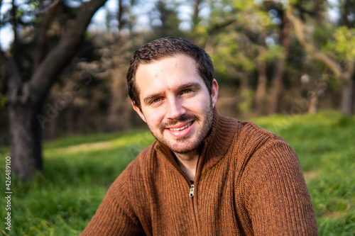 Photo of a young and attractive man sitting in the park during a sunny day and smiling