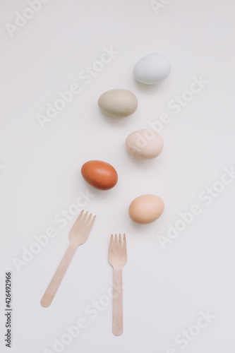 Chicken eggs of natural shades and colors and wooden fork  bamboo cutlery on white background. Healthy organic food  natural farmer s products  eco-friendly 