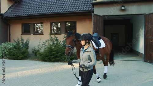 Woman leading horse out of stable.